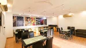 A restaurant with multiple tables and chairs, ceiling fans, and wall-mounted air conditioning units. - Fabhotel The Royal Oak (Gurugram)
