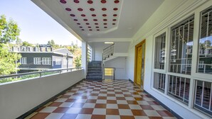 A corridor with a checkered floor, a staircase, and large windows with a view of buildings outside. - FabHotel Greenwood Stays (Ootacamund)