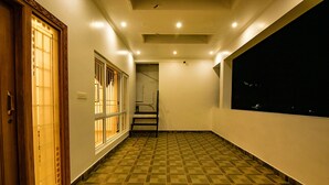 A hallway with a checkered floor, a wooden door with a traditional design, and a large window on the right. - FabHotel Greenwood Stays (Ootacamund)