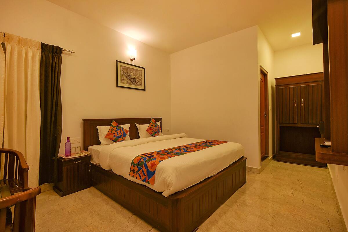 Quarto de hotel com cama, mesas de cabeceira, uma cadeira, guarda-roupa de madeira e um quadro na parede.
