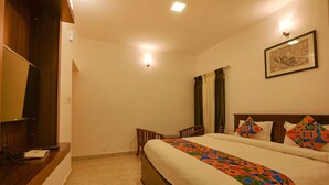 A hotel room with a bed, a desk, a chair, and a television. - FabHotel Greenwood Stays (Ootacamund)