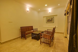 A room with a wooden bench, a small table, and chairs. There is a framed picture on the wall. - FabHotel Greenwood Stays (Ootacamund)
