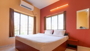 Un grand lit avec du linge de lit blanc, deux fenêtres avec des rideaux, une table de chevet et un miroir fixé au mur.