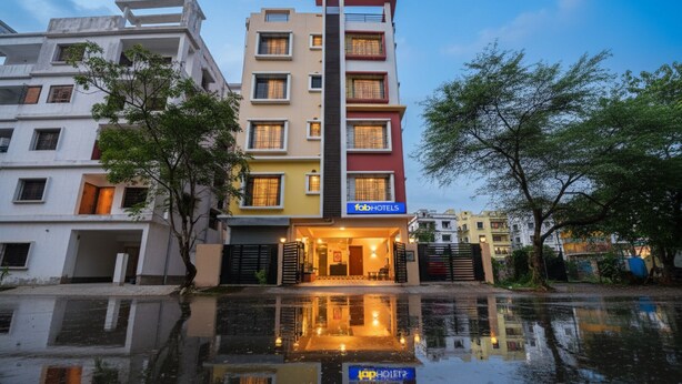 Un hôtel à plusieurs étages, avec une enseigne indiquant « fab hotels », une surface d’eau réfléchissante devant et des arbres tout autour.