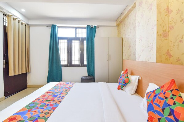 Habitación de hotel con cama, ventana con cortinas, armario y pared con papel tapiz floral.