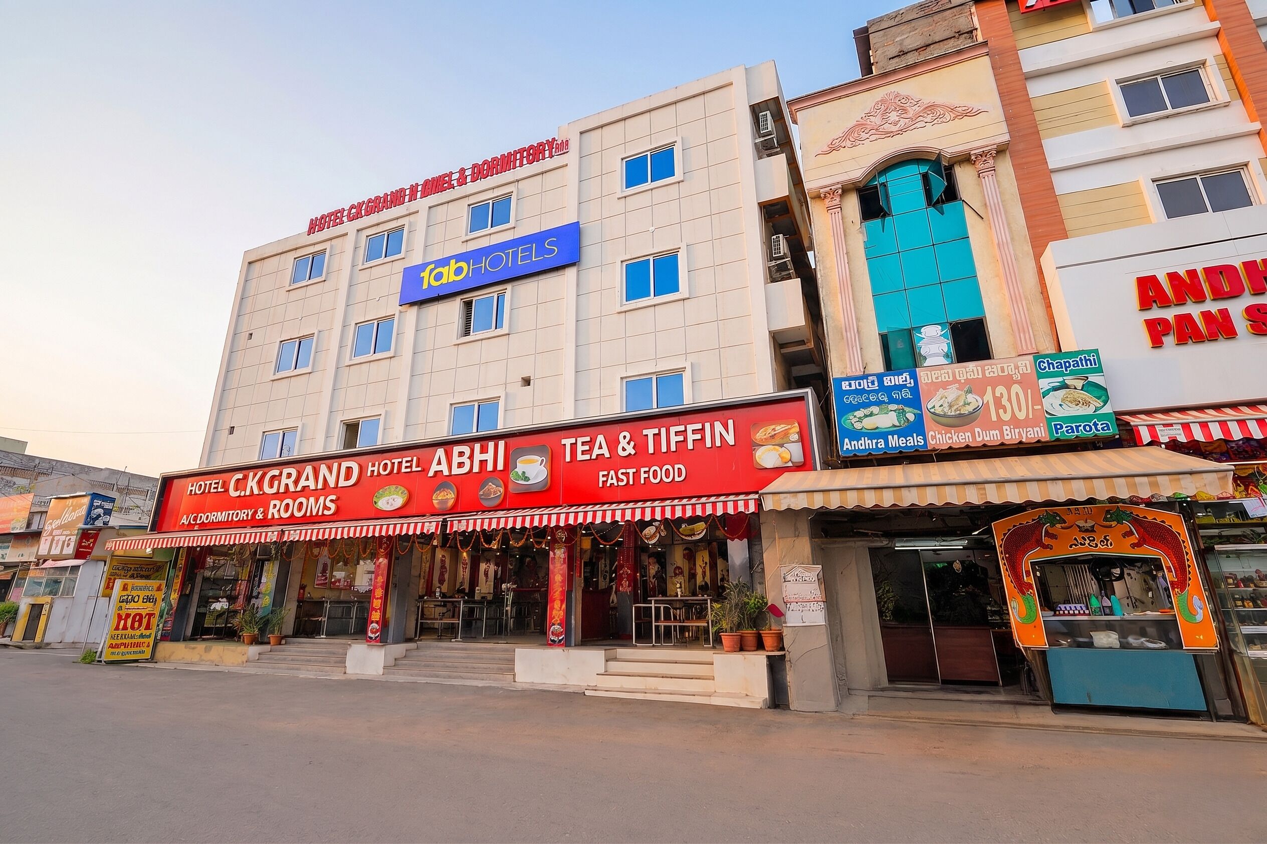Un hotel con un letrero que dice 'ABHI TEA & TIFIN FAST FOOD' y 'HOTEL C.K.GRAND A/C DORMITORIOS Y HABITACIONES'.