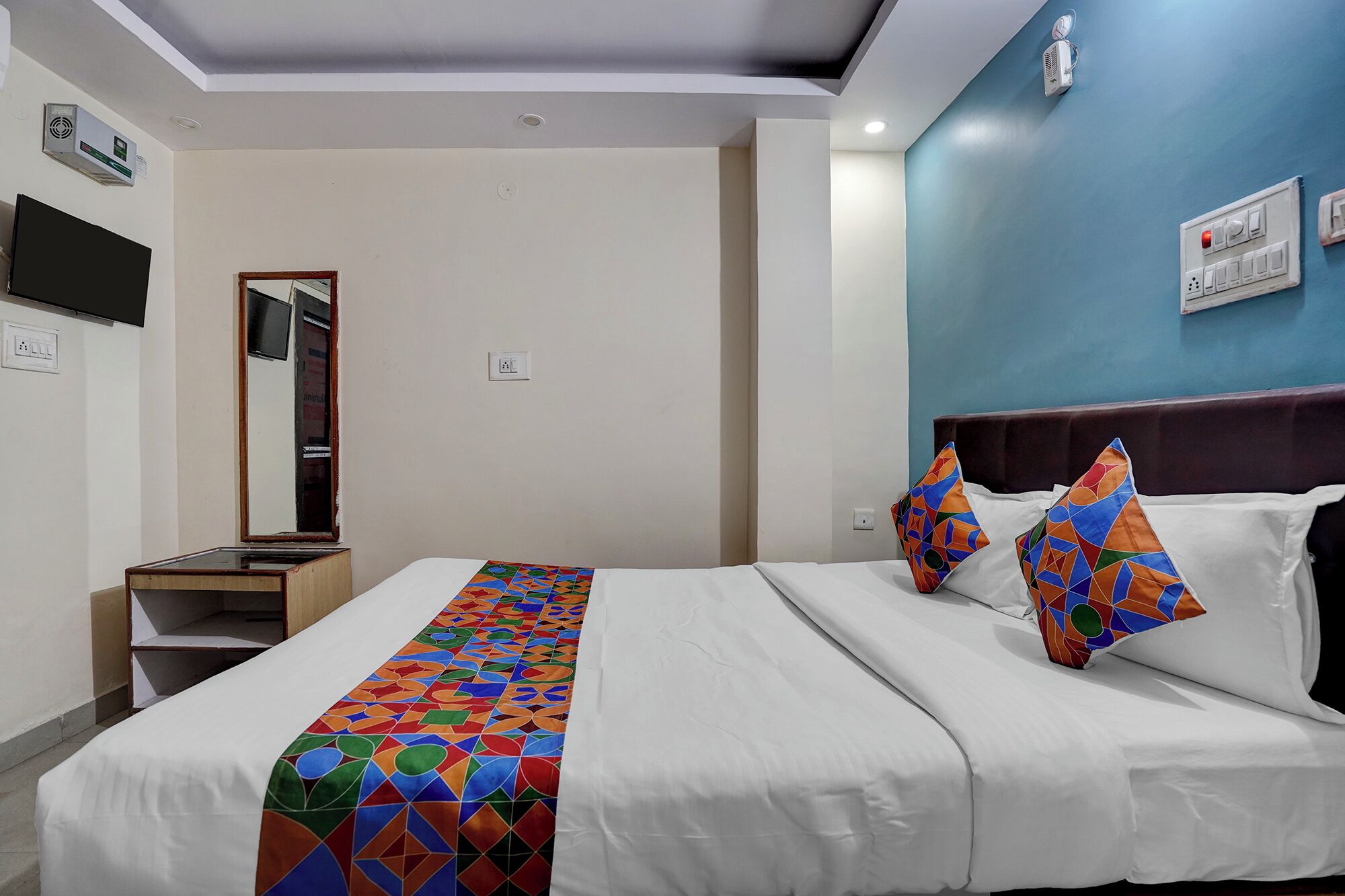 Een hotelkamer met een bed, een televisie, een spiegel en een wandairconditioner.