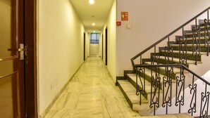 Um corredor com piso de mármore que leva a uma escadaria com grades de metal ornamentadas.