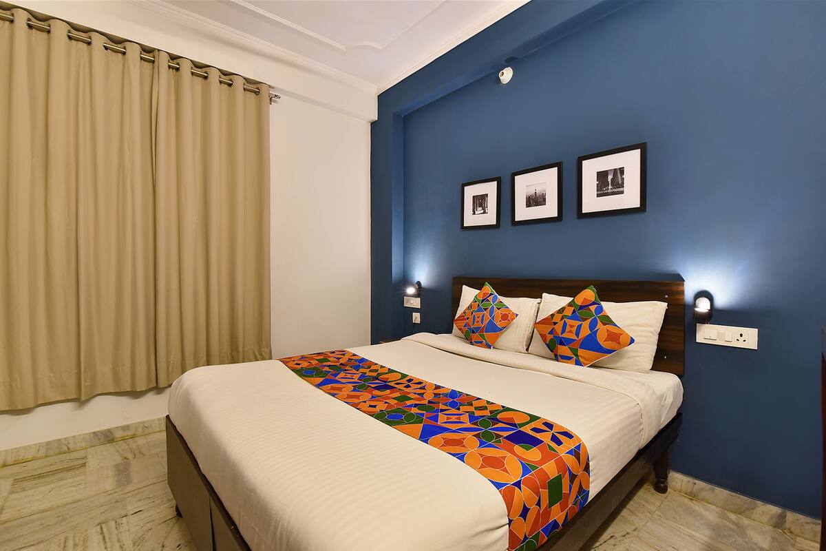 A neatly made bed with a colorful geometric-patterned bedspread, a wooden headboard, and three framed pictures on the wall.