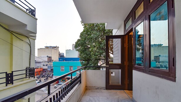 Uma varanda estreita com grade de metal, uma porta que dá para um quarto e vista para um horizonte urbano com edifícios e uma árvore.