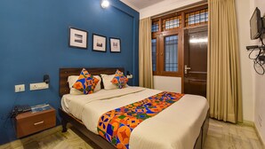 Quarto com cama, mesa de cabeceira, televisão na parede e janela com cortinas.