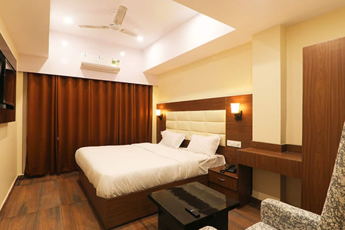 Una habitación de hotel con una cama, un escritorio, una silla, un ventilador de techo y un televisor montado en la pared.