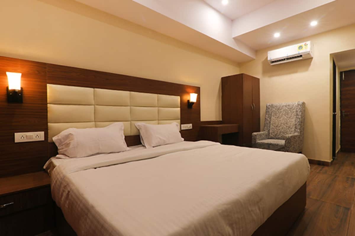 Habitación de hotel con una cama grande, cabecera de madera, dos luces fijadas a la pared, un armario, una silla y un equipo de aire acondicionado.