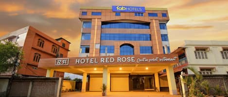 Um hotel com fachada moderna, um letreiro chamativo para 'Hotel Red Rose' e um restaurante 'Cartio point' indicado na entrada.