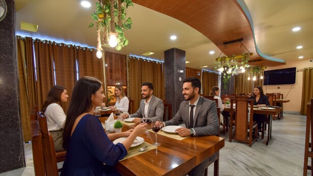 A restaurant with wooden tables and chairs, hanging plants, and a marble floor. - Fabhotel Red Rose (Guwahati)
