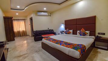 A hotel room with a large bed, a sofa, a desk, and a ceiling fan.