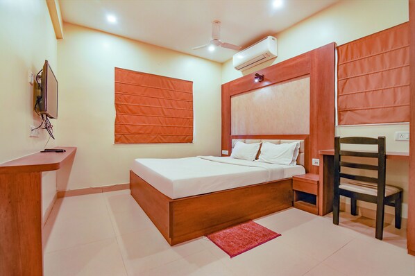 A bedroom with a wooden bed, a desk, a chair, and a TV mounted on the wall.