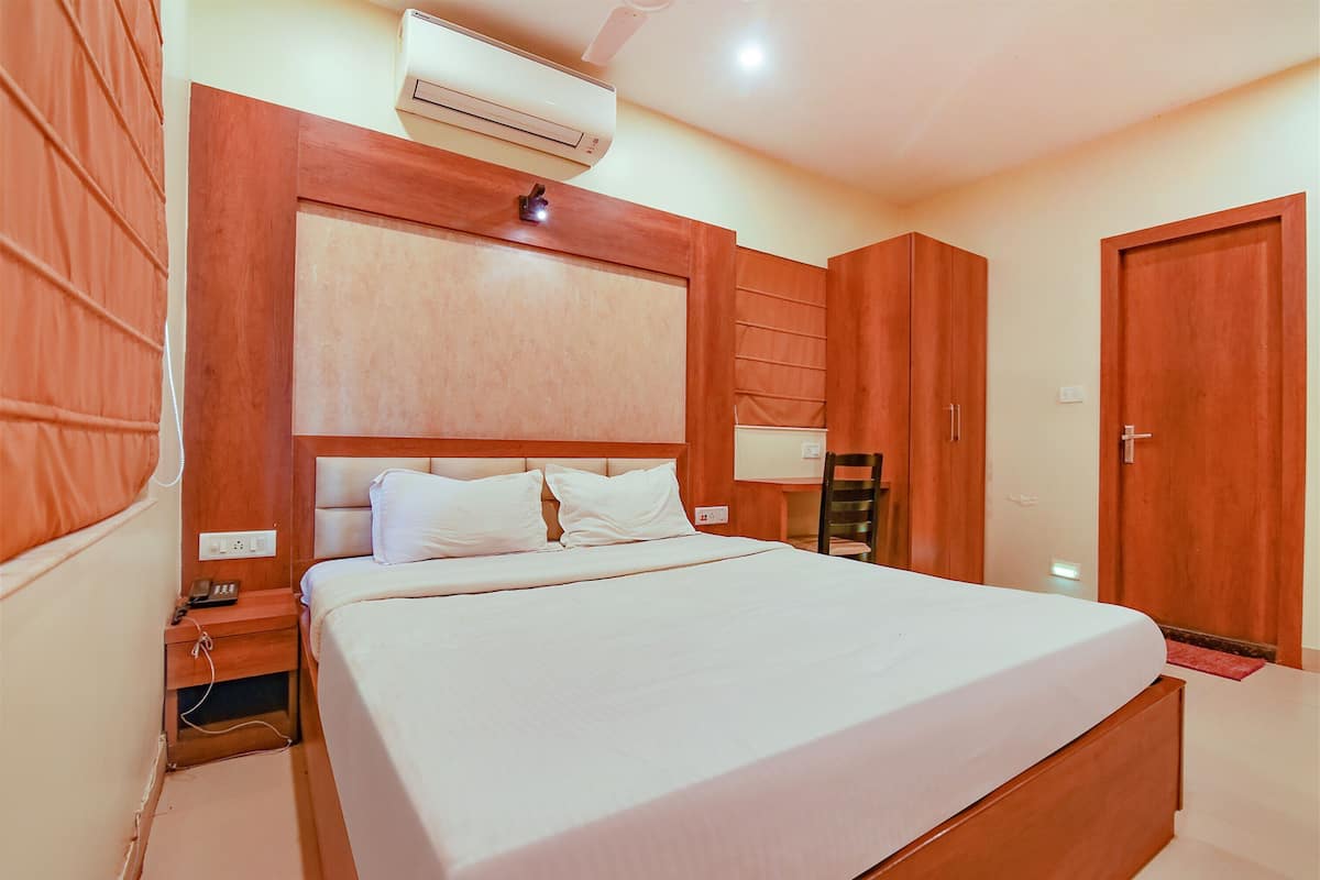 Una habitación de hotel con una cama grande, cabecera de madera, aire acondicionado, una mesita de noche con teléfono y un armario.