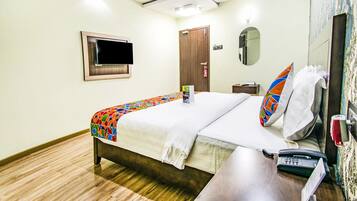 A hotel room with a bed, a bedside table with a phone, a TV mounted on the wall, a door, and a mirror.