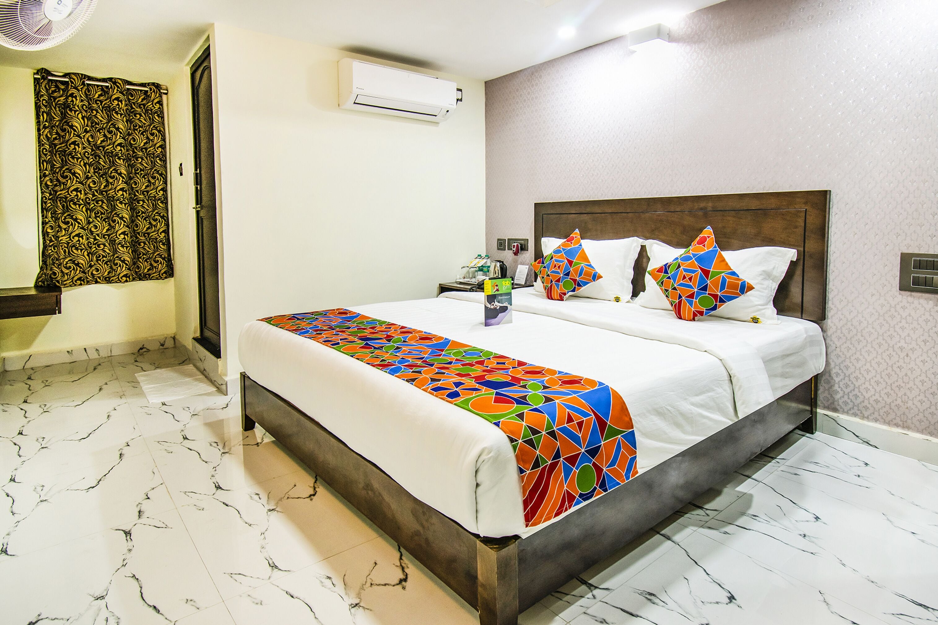 A hotel room with a bed, a nightstand, an air conditioner, a patterned curtain, and a marble floor.