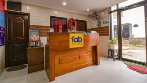 A hotel reception desk with a sign reading "fab hotels," a door, a fan, and a view through the glass door. - Fabexpress Royal Stays (Rishikesh)