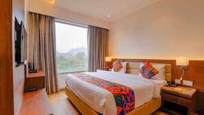 Una habitación de hotel con una cama grande, televisión, mesita de noche y ventana con cortinas.