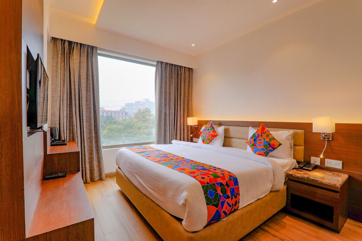 Una habitación de hotel con una cama grande, televisión, mesita de noche y ventana con cortinas.