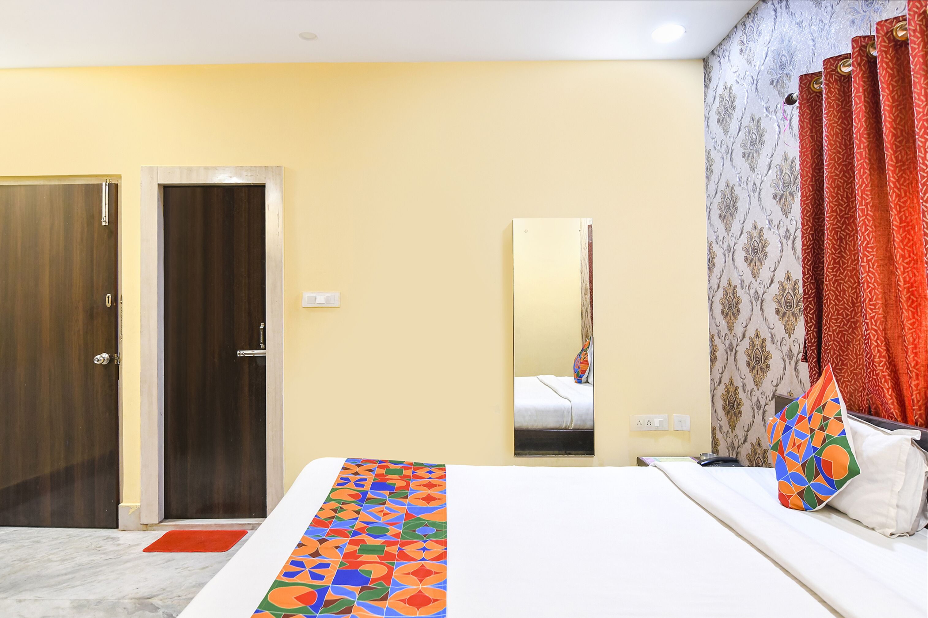 Ein Hotelzimmer mit einem Bett, einem Spiegel, einer Tür und einem gemusterten Teppich.
