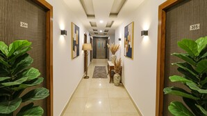 A hotel hallway with numbered doors, artwork, and potted plants. - FabHotel Dolphin International (New Delhi)