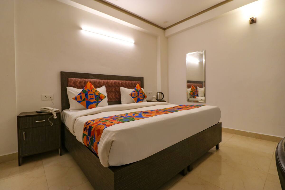 A neatly made bed with a colorful blanket, a bedside table with a phone, and a mirror on the wall.