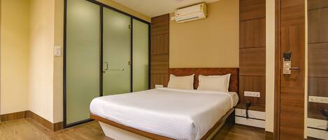 A modern hotel room with a large bed, a ceiling fan, an air conditioning unit, and a sliding door closet.