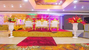 Un escenario con sillas blancas y una alfombra roja, rodeado de arreglos florales y un suelo con diseño.