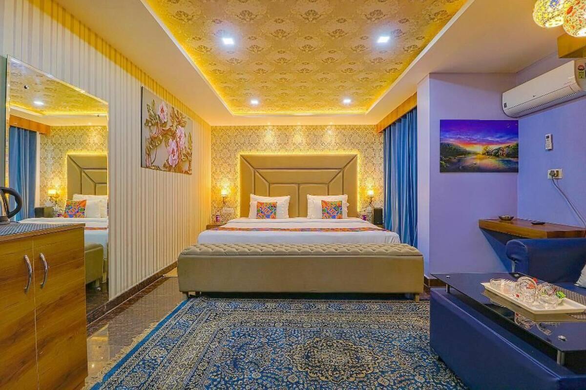 Ein Hotelzimmer mit einem großen Bett, einem Schreibtisch, einem Sessel, einem Kleiderschrank, einem Spiegel und einer Decke mit floralem Muster.