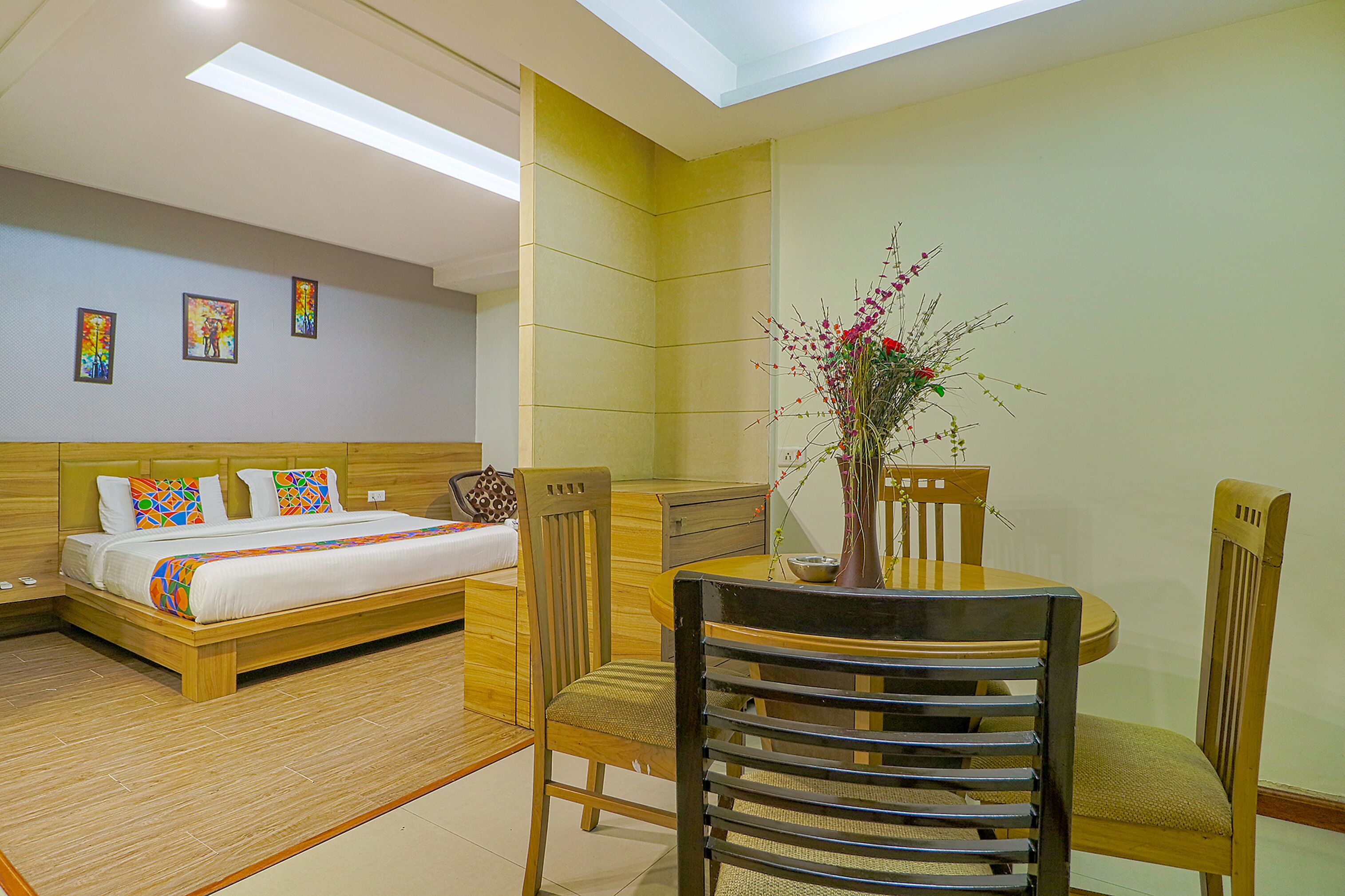 Habitación de hotel con cama, una mesa de comedor con sillas, un florero con flores y cuadros en la pared.