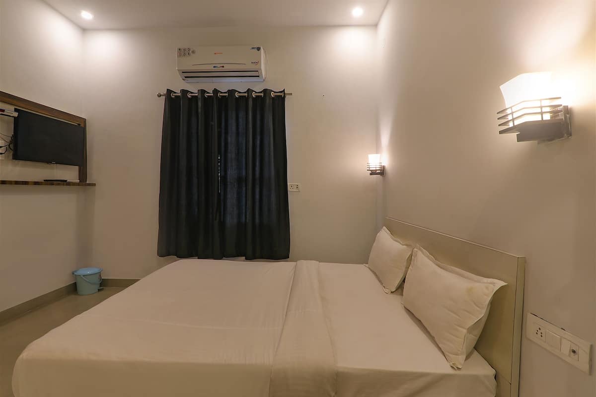 Una habitación de hotel con una cama, un televisor en la pared, aire acondicionado y una lámpara de pared.