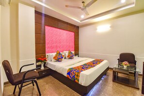 A hotel room with a bed, a chair, a small table, and a ceiling fan.