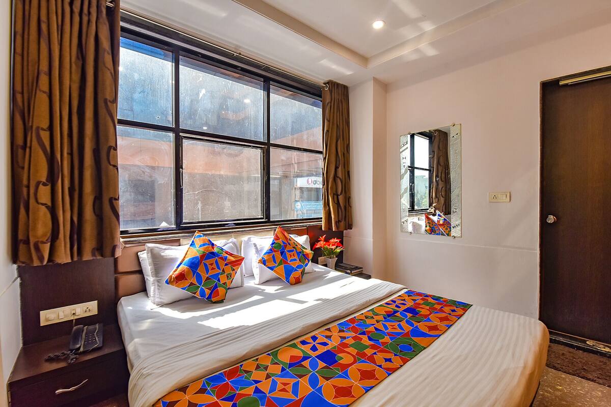 Habitación de hotel con una cama grande, un teléfono en la mesita de noche, una ventana con cortinas y un espejo en la pared.