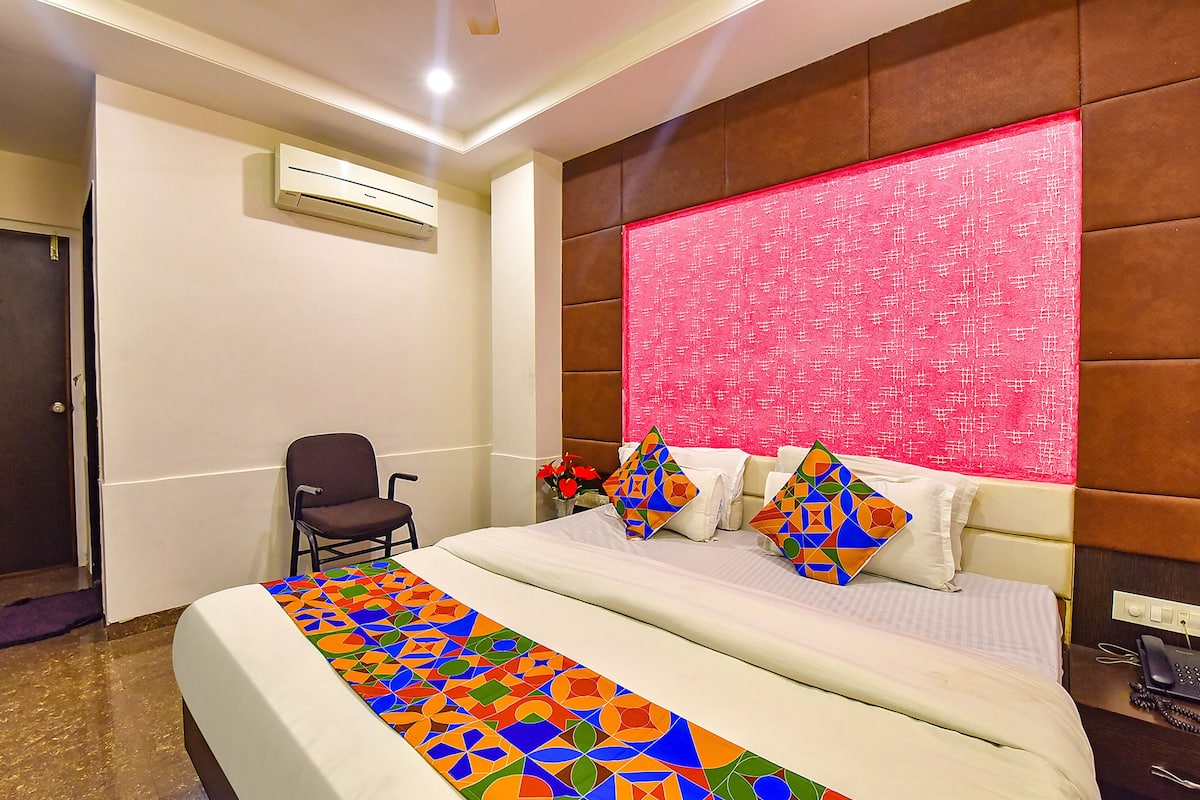 Una habitación de hotel con cama, una silla, una mesita de noche con teléfono y un equipo de aire acondicionado en la pared.