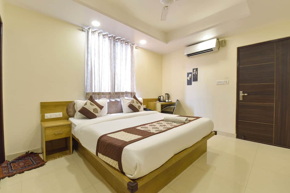 Une chambre d’hôtel bien aménagée, avec un grand lit, une table de chevet, un bureau avec une chaise, un climatiseur et une armoire.