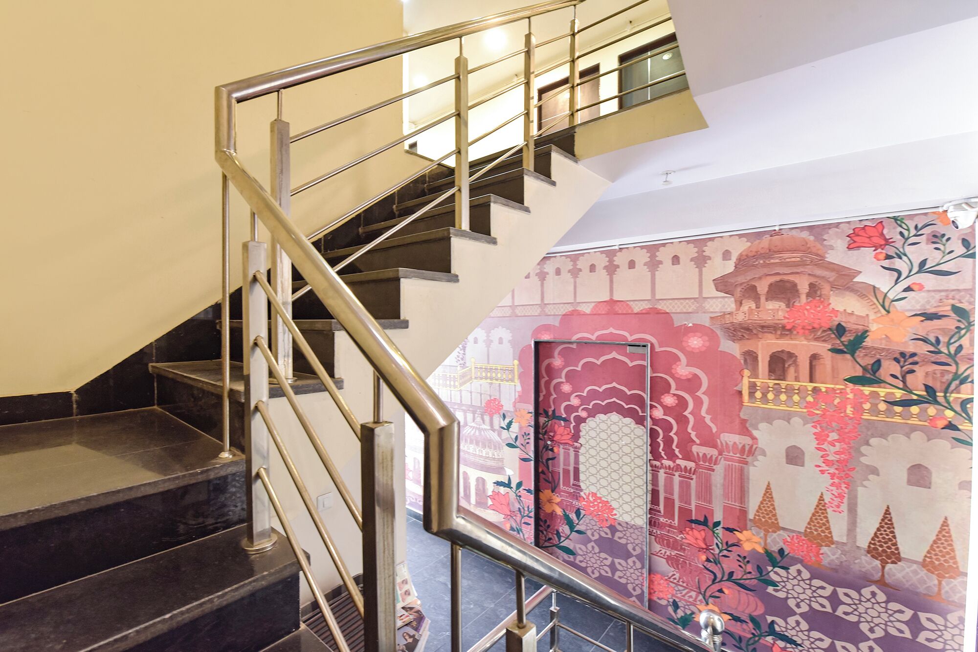 A staircase with a metal railing and a mural with architectural designs.