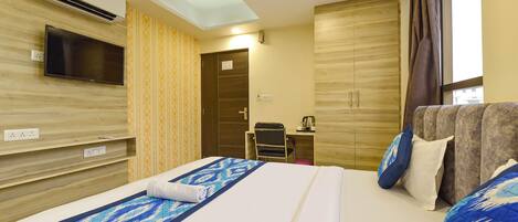 A hotel room with a bed, a TV mounted on the wall, a desk with a chair, and a wardrobe.