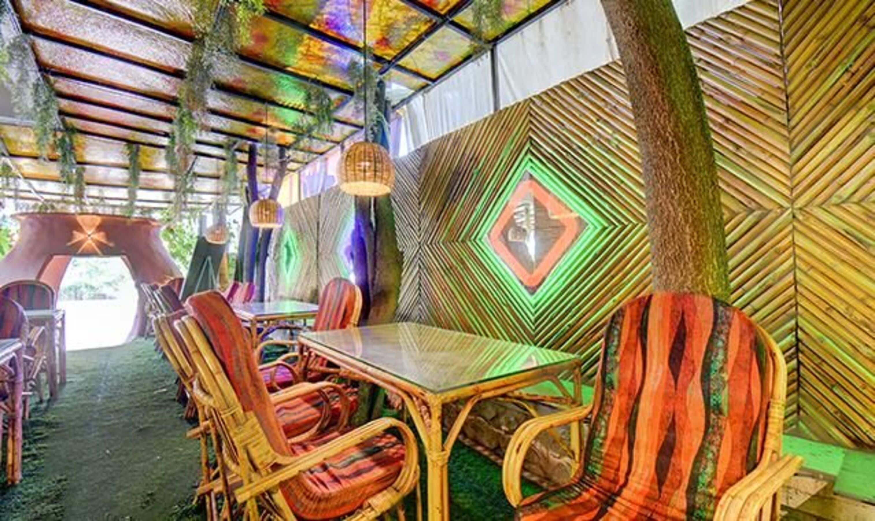 A rustic dining area with a wooden table and wicker chairs, surrounded by a colorful, geometric-patterned wall.