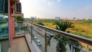 Un balcón con vistas a un paisaje urbano, una calle con coches y un campo verde.