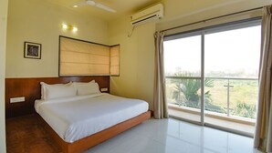 Habitación de hotel con una cama grande, ventilador de techo, aire acondicionado y vistas a zonas verdes por la ventana.