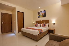 A hotel room with a large bed, a headboard with wall-mounted lights, a painting above the bed, and a wooden door. - Fabhotel Royal International (Mumbai)
