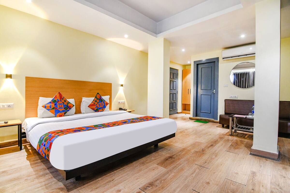 A hotel room with a bed, bedside tables, a desk, and an air conditioning unit.