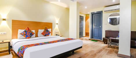 A hotel room with a bed, bedside tables, a desk, and an air conditioning unit.