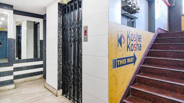 Entrada de hotel con una puerta negra, una pantalla digital y un cartel que indica el camino a Koshe Koshala.