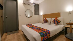 Ein Hotelzimmer mit einem Bett, einem Holzkopfteil, einem Nachttisch mit einem Sessel, einem runden Spiegel an der Wand und einer Klimaanlage.