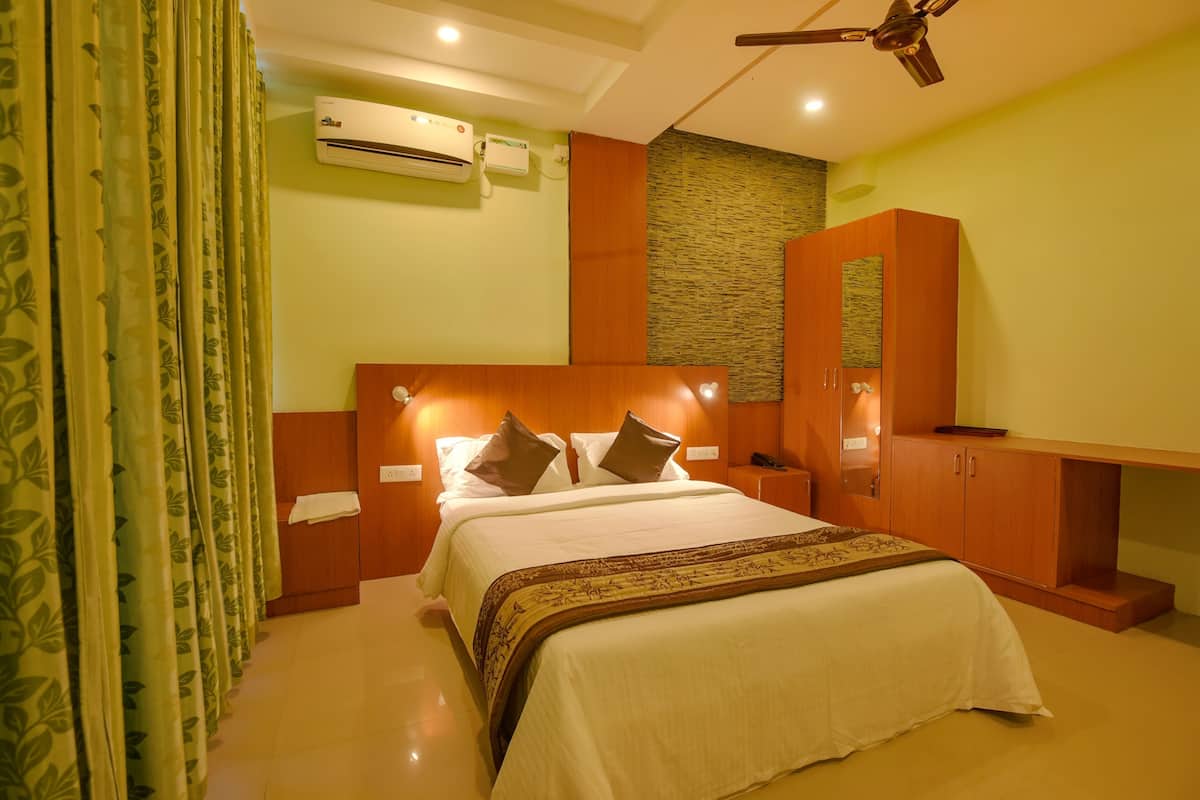 Quarto de hotel com cama, escrivaninha, guarda-roupa, ar condicionado e ventoinha no teto.